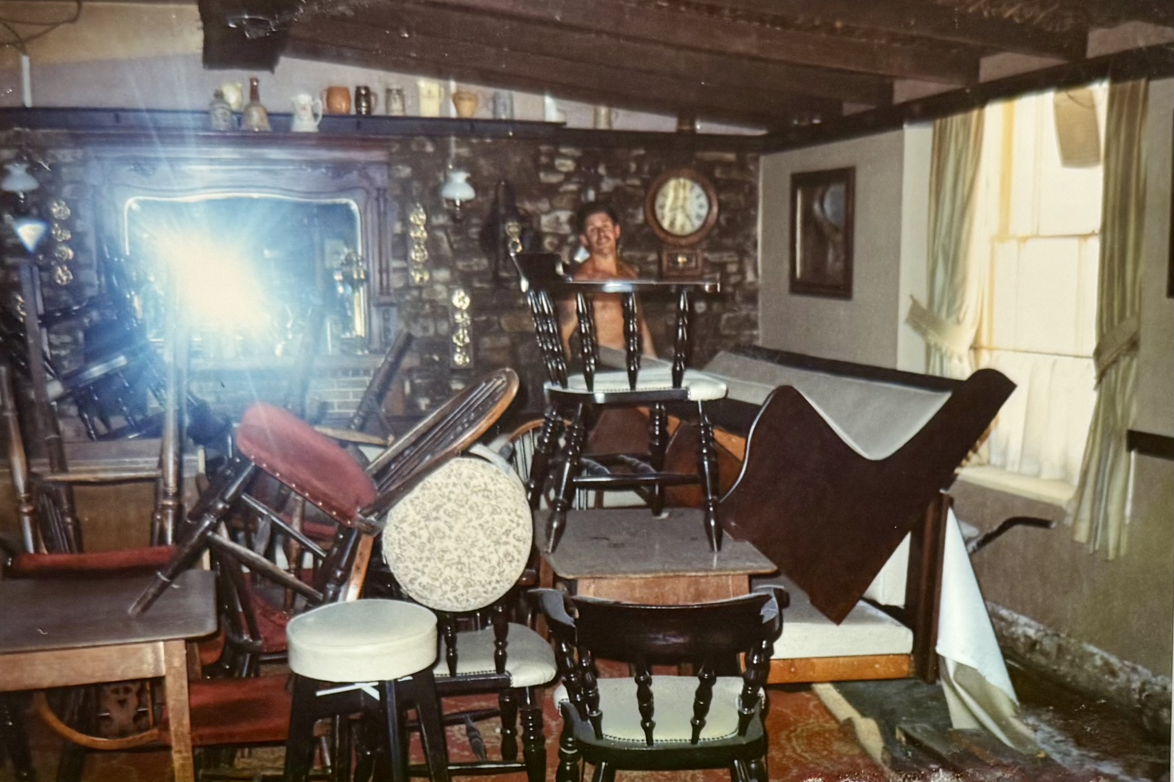 More tables and chairs stacked in the Bar area, including the banquet seating which originally went around the edge of the room. In the background, you can see a man in front of the fireplace wall, which today is painted white.