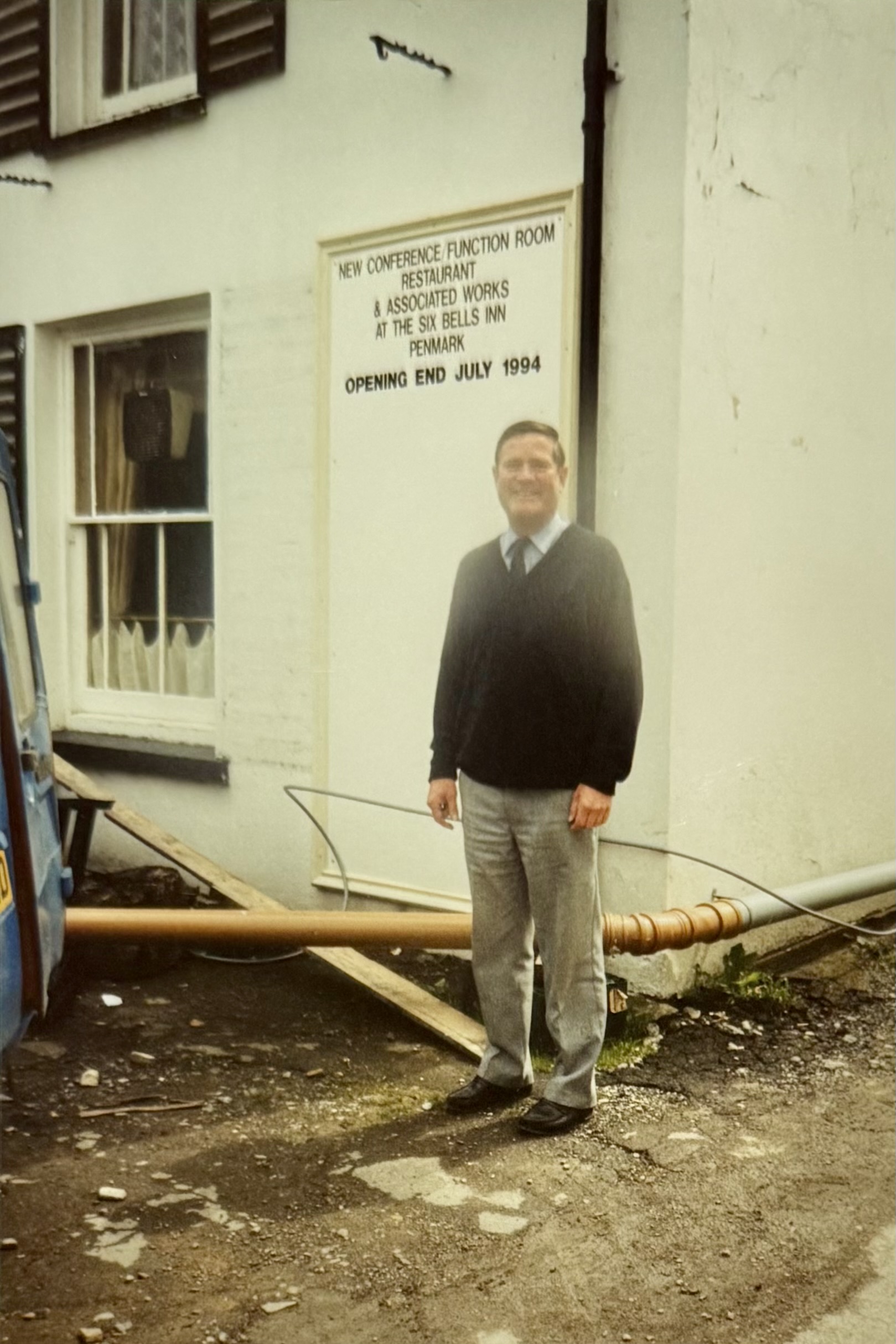 A man stood outside the pub, by the Bar window. You can read the sign behind him announcing the upcoming opening of the Function Room and Restaurant. You can see construction materials on the floor around him, and the previous bar window which had a fan within the window panes.