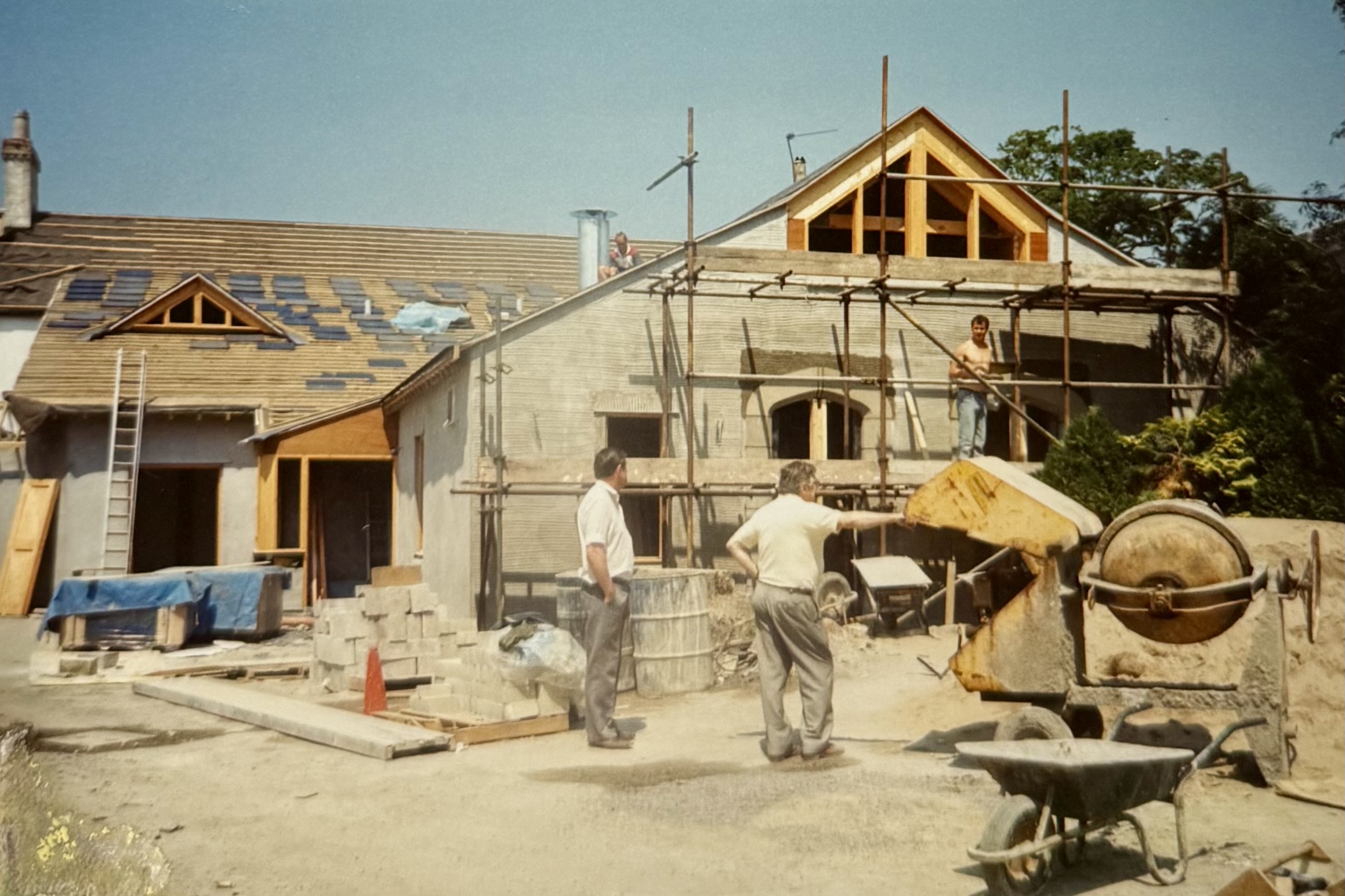 Two men standing, watching the work take place at the back of the pub. 