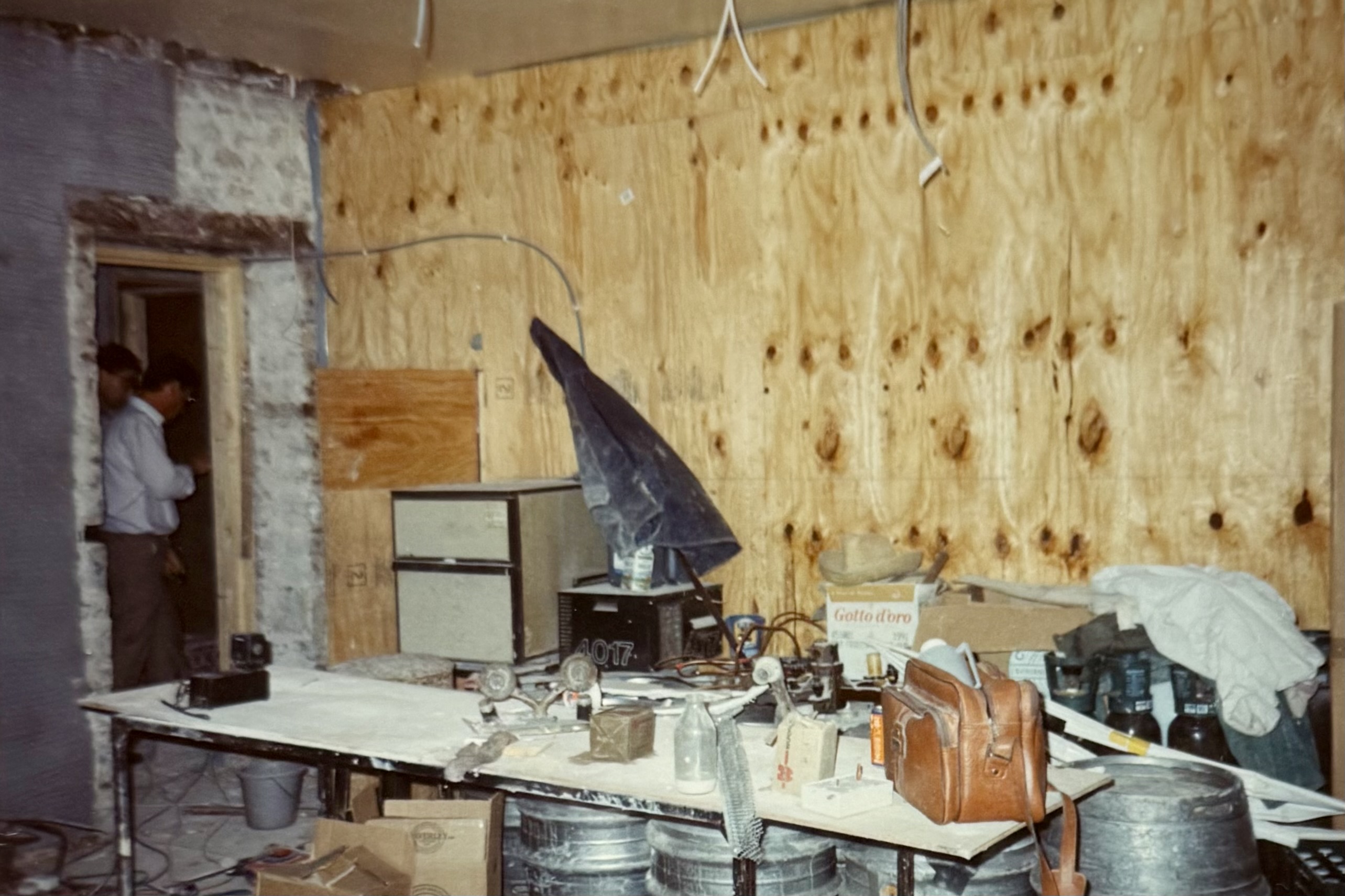 A temporary cellar area, with a table, filing cabinet, a parasol, and all sorts of things on the table.