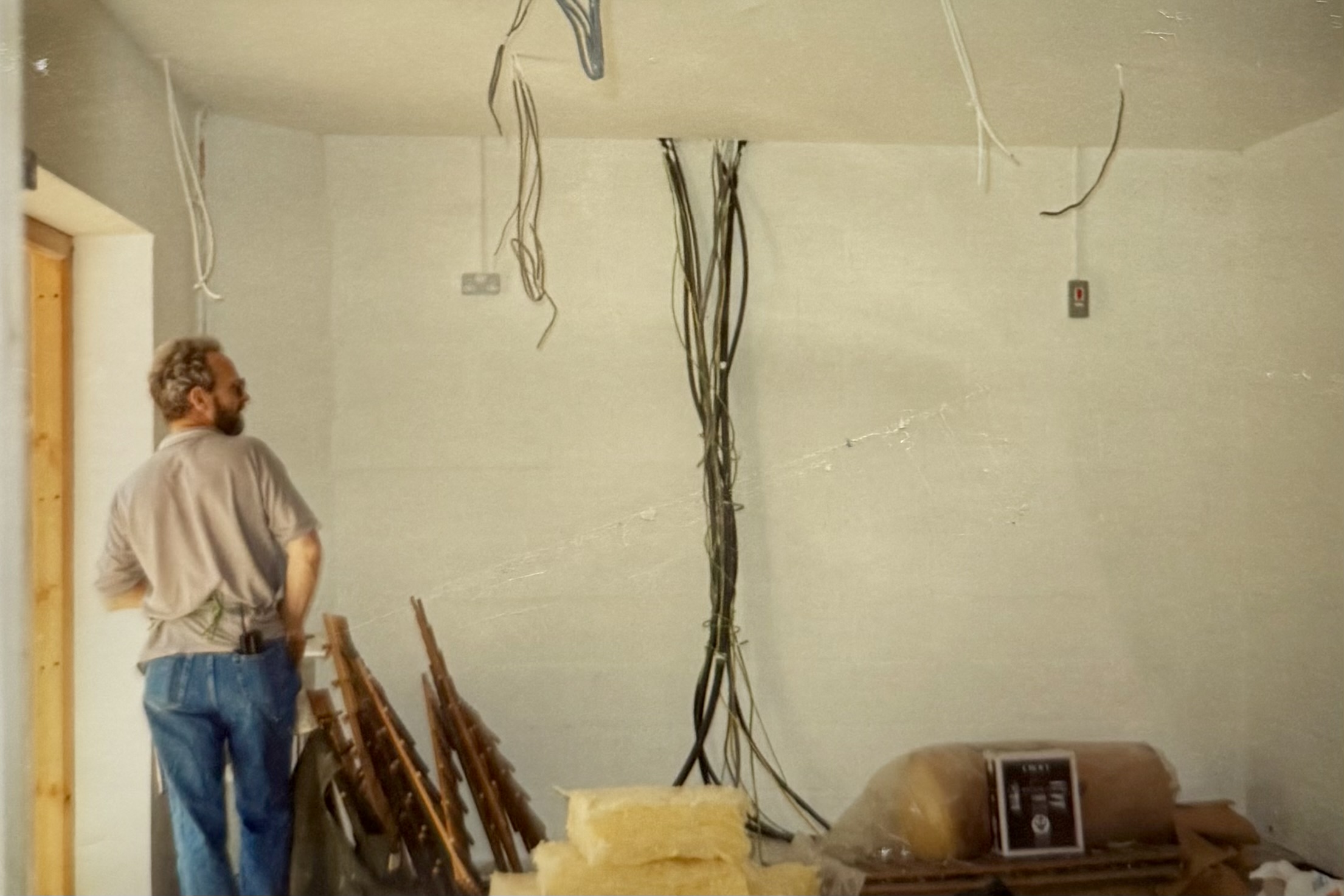 A man in a room with lots of exposed wiring running down the walls and from the ceiling.