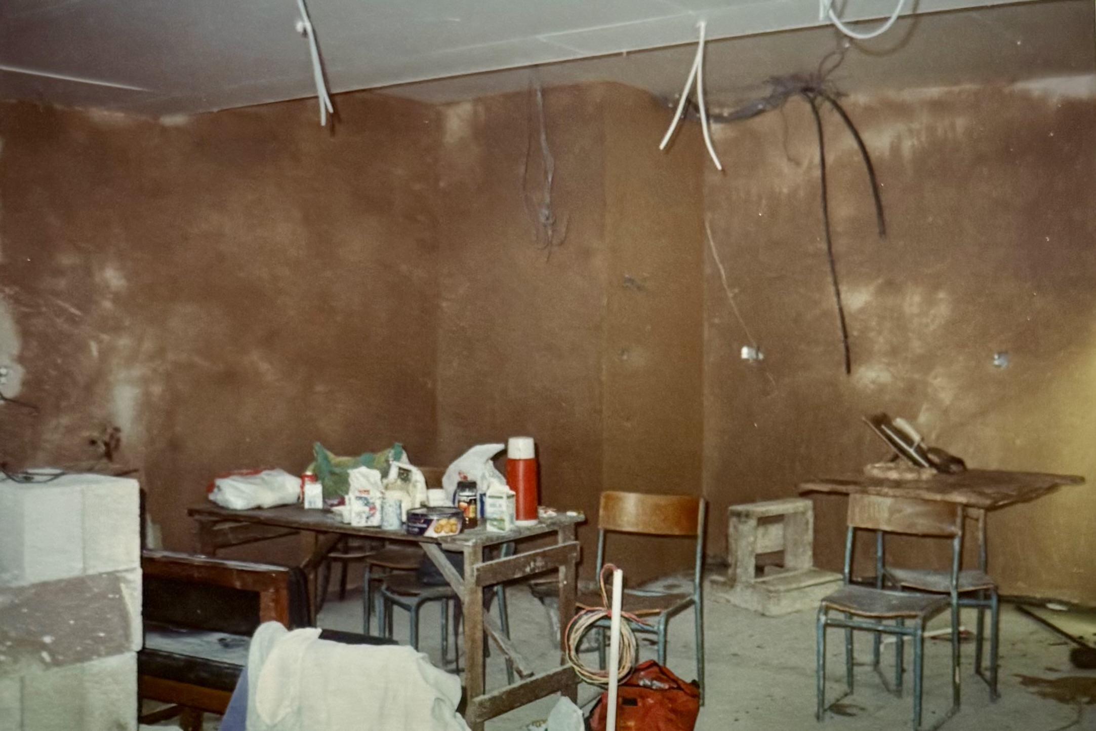 Some tables and chairs in a room with freshly plastered walls and wiring hanging from the ceiling.