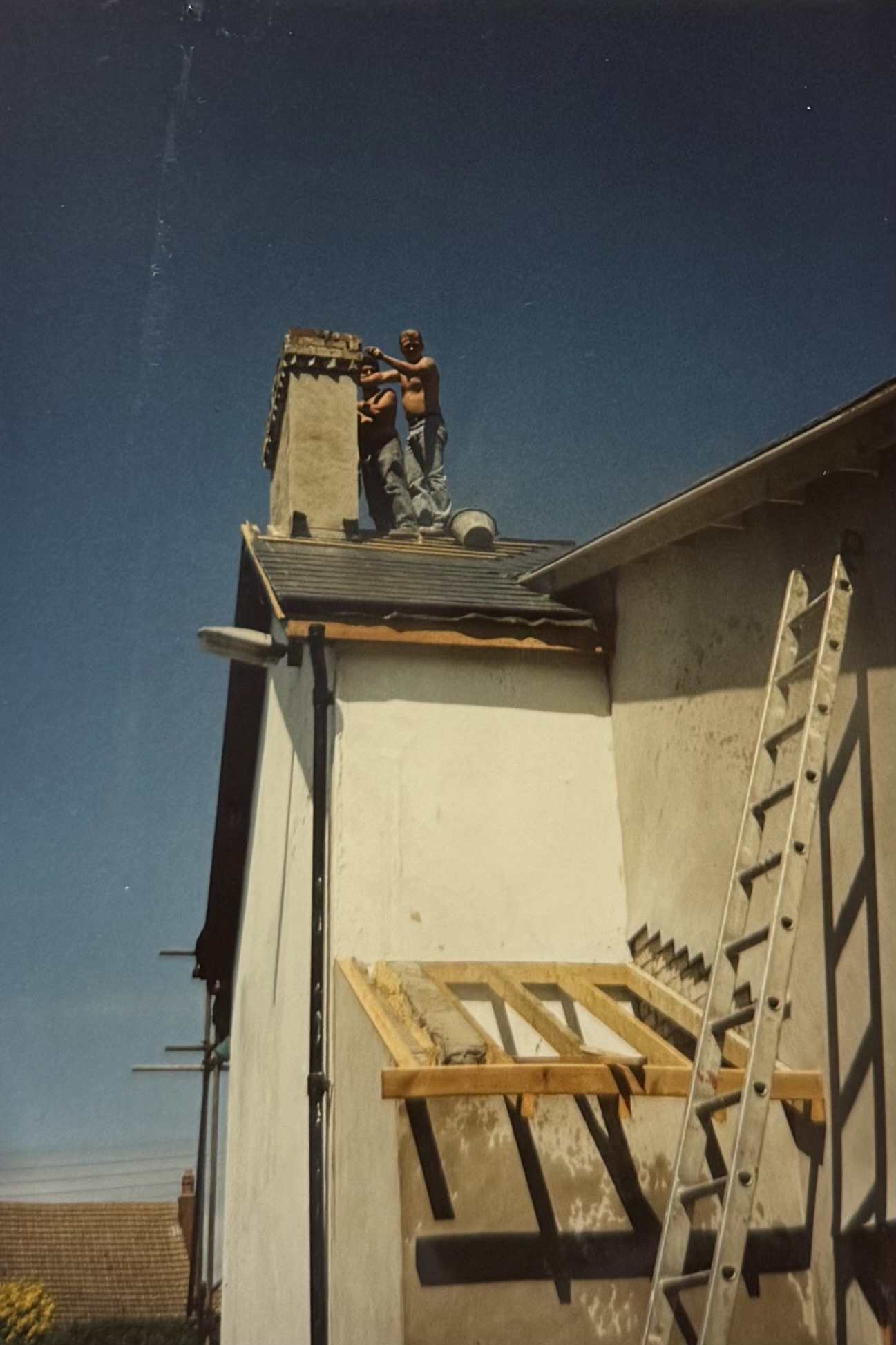 Two men on the roof, working on the chimney. The building below them is mid-renovation.