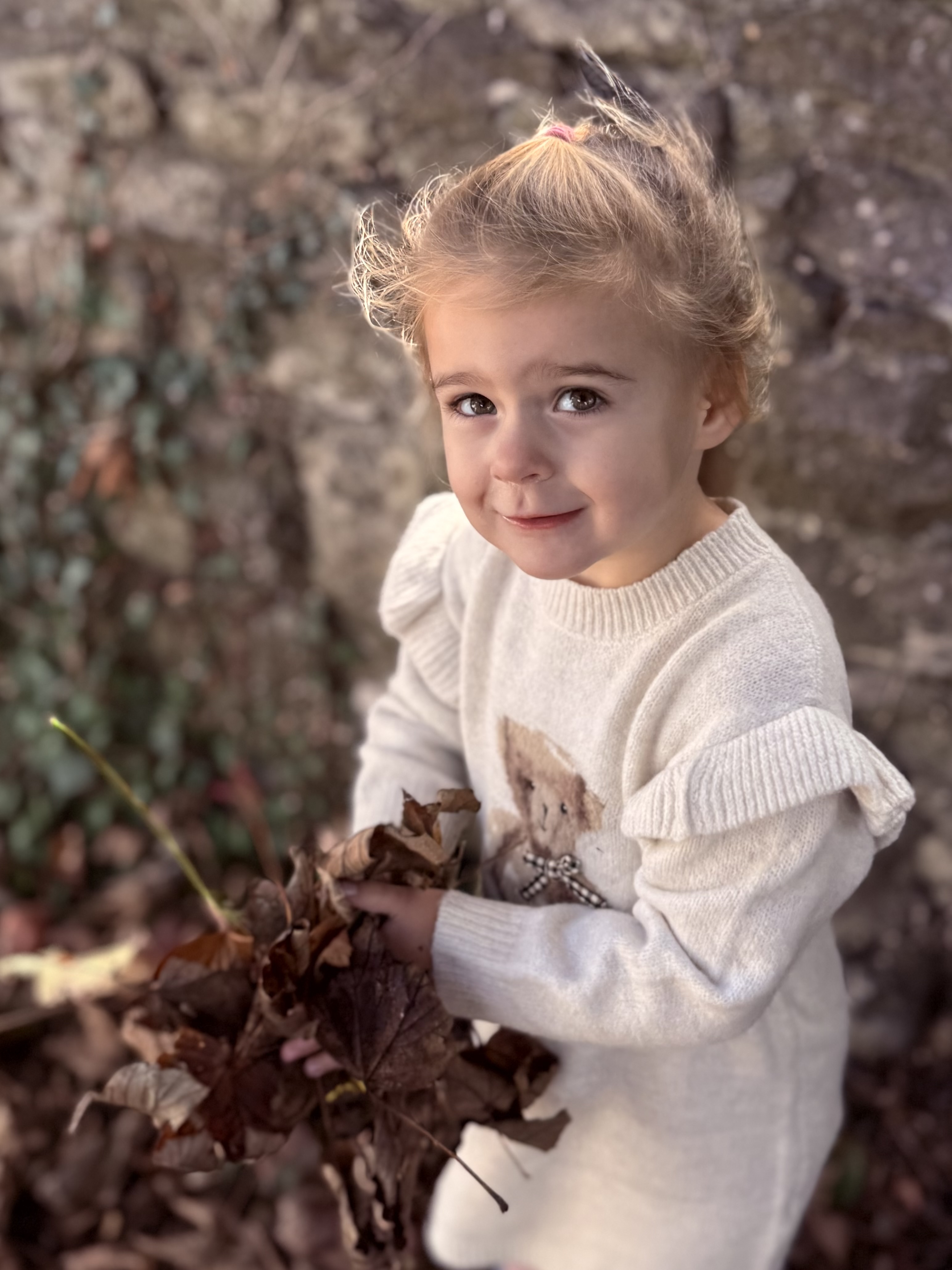 Cassie, 2 and half years old, smiling while holding a pile of Autumn leaves.