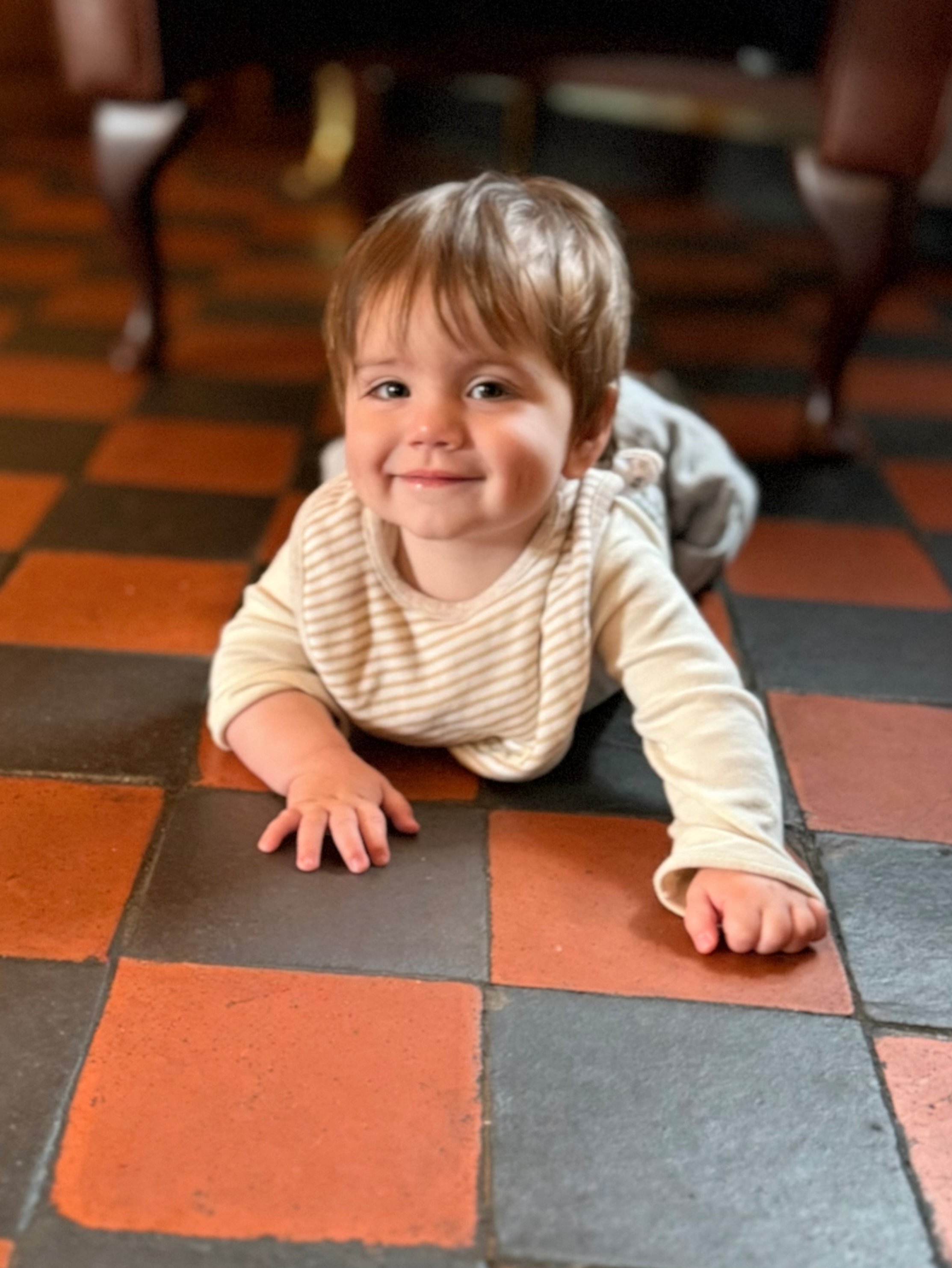 George, 10 months old, smiling, lying on his front on the floor of the Bar area of the Six Bells. 